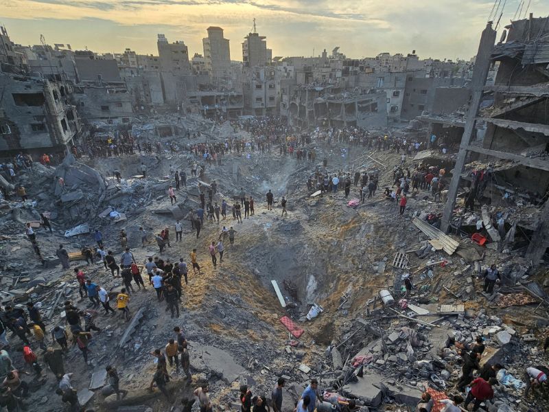 Urban devastation following Israel Qatar airstrike, with civilians inspecting massive crater and collapsed buildings in a war-torn zone."